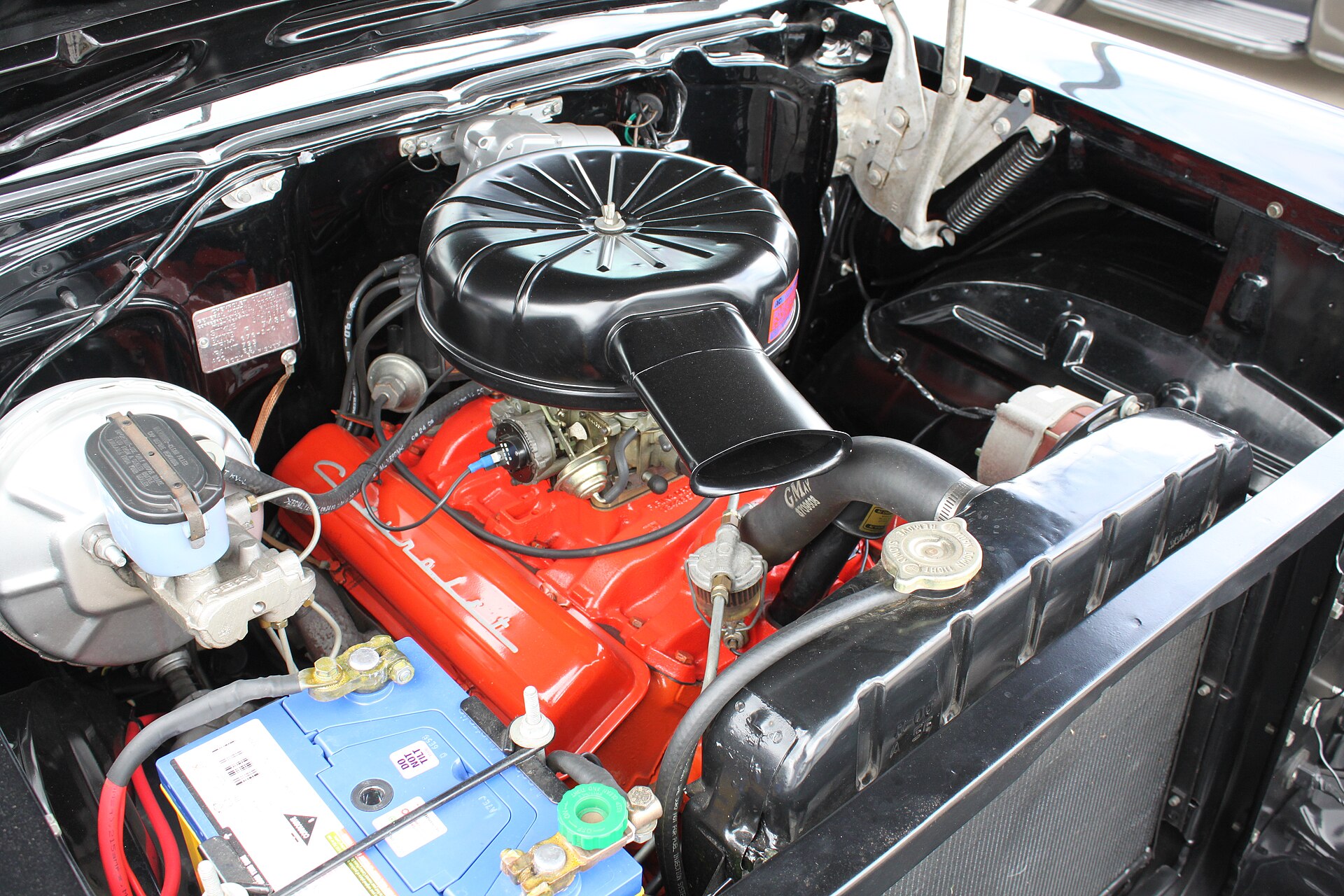 A 1957 Bel Air engine bay with V8, air cleaner, hoses, battery, and radiator visible.